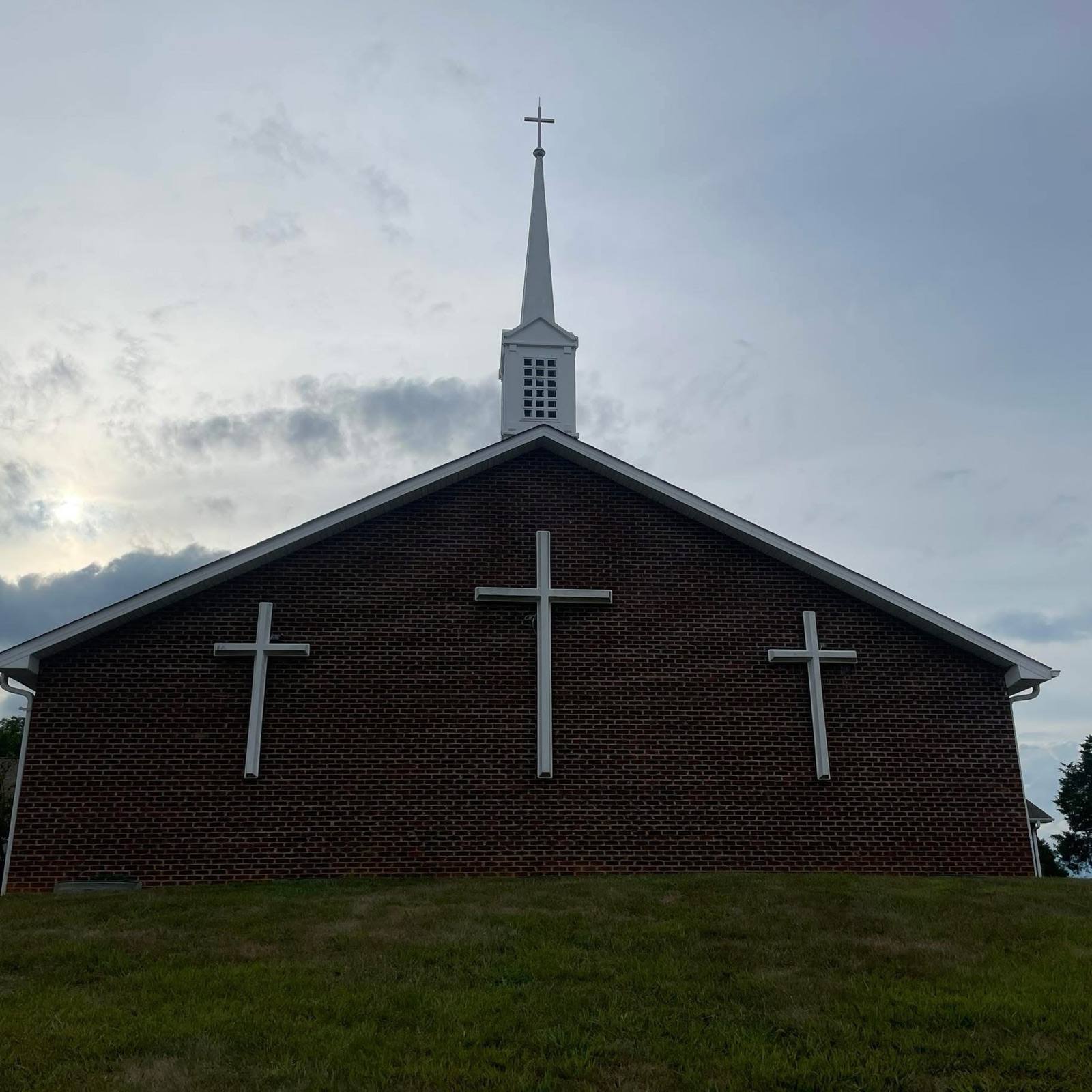 Second Baptist Church — brick sanctuary with three crosses and a white steeple against an evening sky